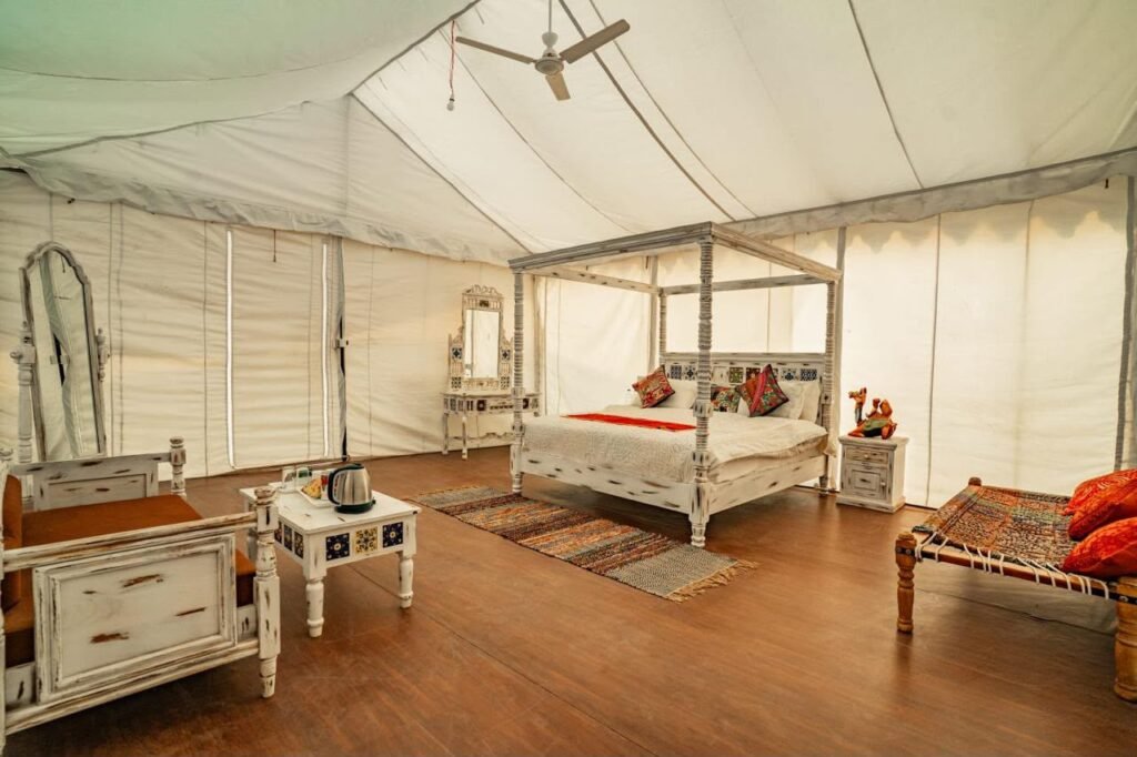 Inside a white canvas tent, a rustic distressed-wood four-poster bed with colorful pillows dominates the room.